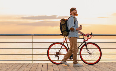 Fototapeta premium handsome bearded man traveling with bicycle in morning sunrise by the sea