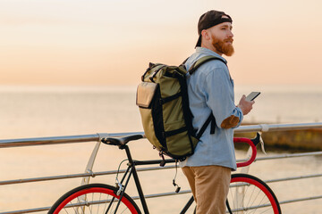 handsome bearded man traveling with bicycle in morning sunrise using phone