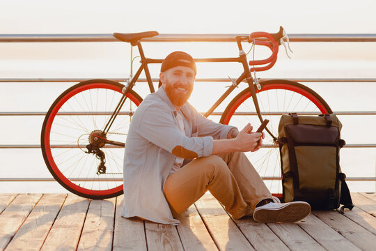 handsome bearded man traveling with bicycle in morning sunrise using phone