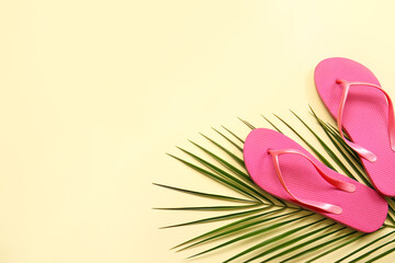 Stylish flip-flops and palm leaf on color background