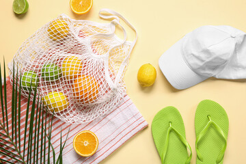 String bag with citrus fruits, towel, cap and flip-flops on color background