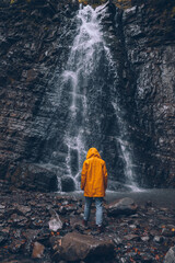 woman in yellow raincoat at autumn waterfall