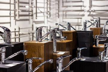 New modern metal water faucets for bathroom on the shop display stands on dark background.