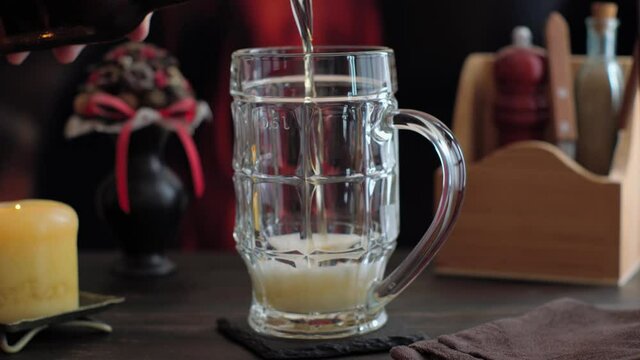 Beer pouring in mug from bottle on table in pub against fireplace