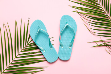 Stylish flip-flops and palm leaves on color background