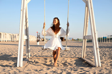 Young Beautiful brunette girl on the beach swinging on a swing