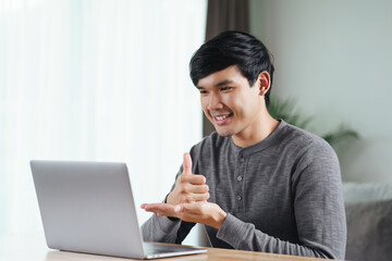 Young Asian man deaf disabled using laptop computer for online video conference call learning and communicating in sign language..