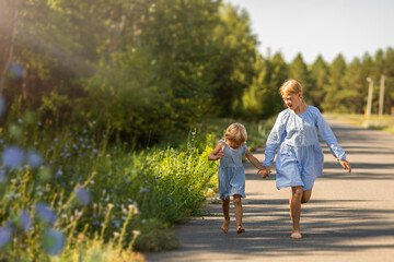 Fototapeta premium Sisters on a walk in the forest hold hands, friendship between girls in the sunset rays of the sun on a meadow with wildflowers