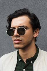 Obraz premium portrait of young man in stylish sunglasses posing near grey wall