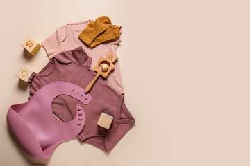 Baby clothes, bib and toys on color background