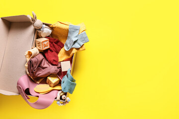 Box with baby clothes, toys and accessories on color background, closeup