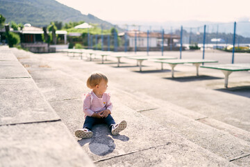 Fototapeta na wymiar Little girl sits on stone steps and looks at tennis tables
