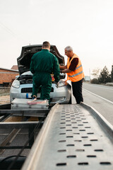 Two road assistant workers in towing service trying to start car engine with jump starter and...