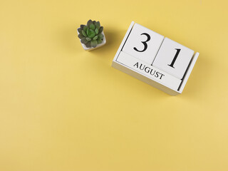 flat lay of wooden calendar with date August 31 and cactus plant pot  on yellow background with...