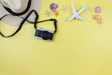 flat lay of camera, straw hat, airplane model with sea shells and starfish on yellow background with copy space. Summer beach vacation background.