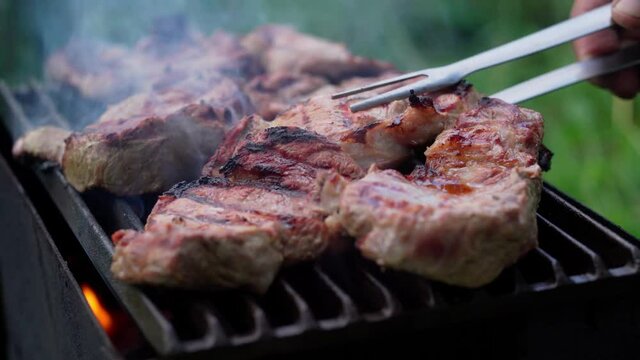 Cooking pork steaks on the barbecue grill at a picnic, close-up
