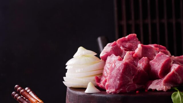 Raw cubed pieces of pork on cutting board with onion on rustic table rotation with copy space