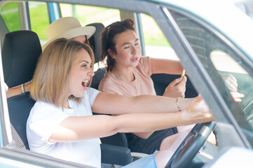Three friends go on a trip. Caucasian women drive in a car and point fingers in surprise.