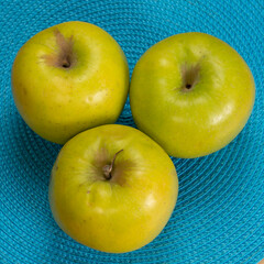 three green apples on a blue woven table matt background