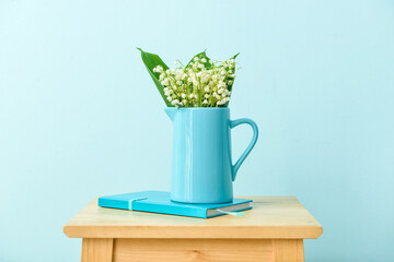 Vase with lily-of-the-valley flowers and notebook on table near color wall