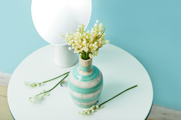 Vase with lily-of-the-valley flowers and mirror on table near color wall