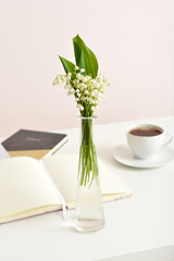 Vase with lily-of-the-valley flowers and books on table