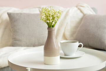 Vase with lily-of-the-valley flowers and cup of coffee on table at home - obrazy, fototapety, plakaty