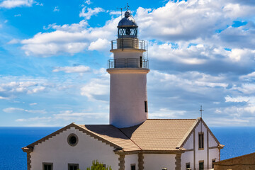 Lighthouse with little houses by the sea with blue sky and clouds.