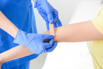 Nurse applying medical patch on young woman's arm in clinic