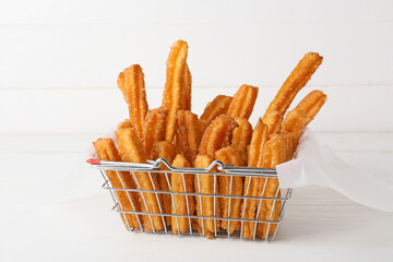 Basket with tasty churros in parchment on light wooden background