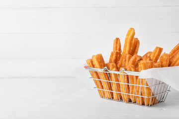 Basket with tasty churros in parchment on light wooden background