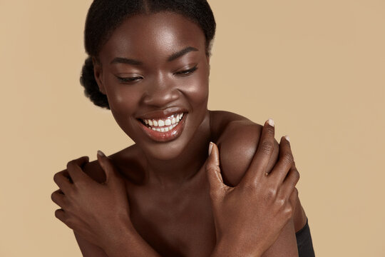 Portrait Close Up Of Beautiful African Girl. Thoughtful Young Woman With Perfect Skin Hug Herself. Concept Of Skin Care. Isolated On Beige Background. Studio Shoot