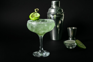 Glass of cold daiquiri cocktail and shaker on dark background