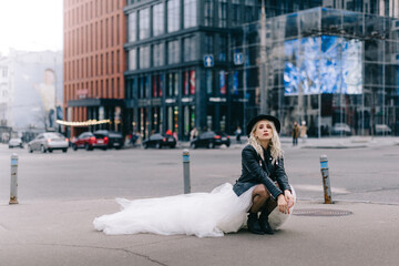 Young bride in black leather jacket sits on his haunches on city street. New York, USA.