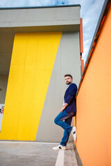 a man in a blue jacket and jeans is pensive and serious, stands against the background of a yellow wall