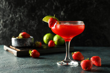 Glass of strawberry daiquiri cocktail, limes and berries on color background