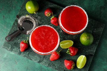 Glasses of strawberry daiquiri cocktail, limes, berries and strainer on color background