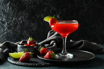 Glass of strawberry daiquiri cocktail and berries on dark background