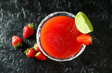 Glass of strawberry daiquiri cocktail and berries on dark background