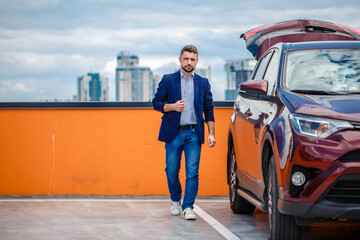 Stylish man in a jacket and blue jeans posing in an open parking lot. Car parking in the background. Business center