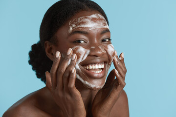 Close up portrait of beautiful black girl wash her face with cleansing face foam. Smiling young...