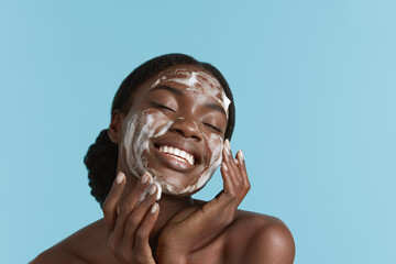 Close up portrait of beautiful black girl wash her face with cleansing face foam. Smiling young...