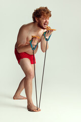 Cute red-headed man in red swimming shorts posing isolated on gray studio background. Concept of sport, humor and body positive.