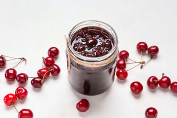 Glass jar of tasty cherry jam on light background