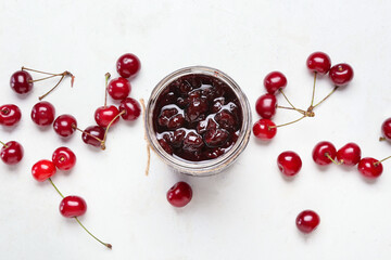 Glass jar of tasty cherry jam on light background