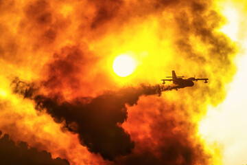 A firefighting plane releases its load of water as it tries to extinguish a fire - obrazy, fototapety, plakaty