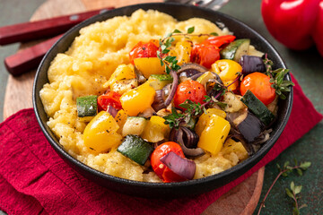 Polenta with stewed vegetables and herbs in a bowl. Polenta with tomatoes, peppers, zucchini, eggplant and thyme. Italian cuisine, vegetarian food.