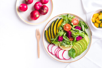 Healthy vegan salad fruits and vegetables with avocado, dragon fruit, radish, pumpkin, tomato, corn salad, lettuce, mizuna and lemon on white background