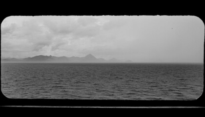 Coast of Komodo through porthole of ship, with stormy skies