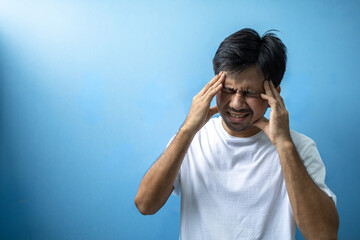 Asian man with headache and stressed because of pain and migraine on blue background 